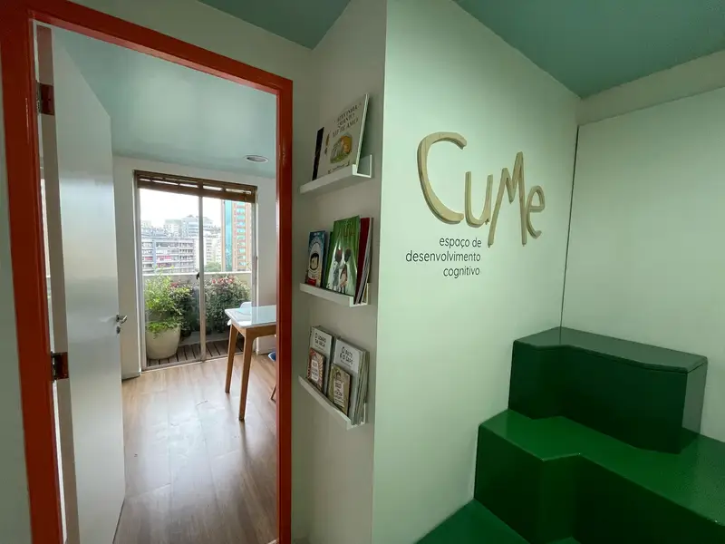Parede com a marca Cume e estante de livros infantis